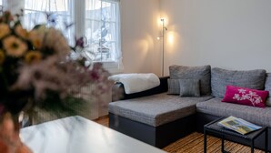 A modern living room with a grey sofa, a small side table, and a window with sheer curtains.
