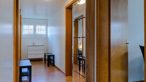 A hallway with a wooden door, a small table, a dresser, and a window with blinds.