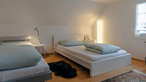 A bedroom with two beds, a bedside table, a lamp, and a window.