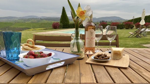 A wooden table set with a tray of strawberries, a bottle of wine, glasses, and a vase with flowers. - Villa with private pool and panoramic view in beautiful Val d'Orcia (San Giovanni d'Asso)