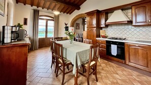 A kitchen with wooden cabinets, a dining table with chairs, a coffee machine, and a view of the outdoors through a window. - Villa with private pool and panoramic view in beautiful Val d'Orcia (San Giovanni d'Asso)