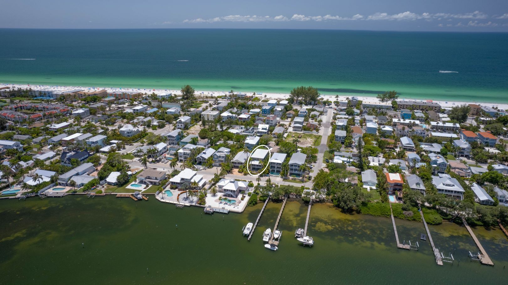 An aerial view of a coastal residential area with houses, a marina, and a beach.