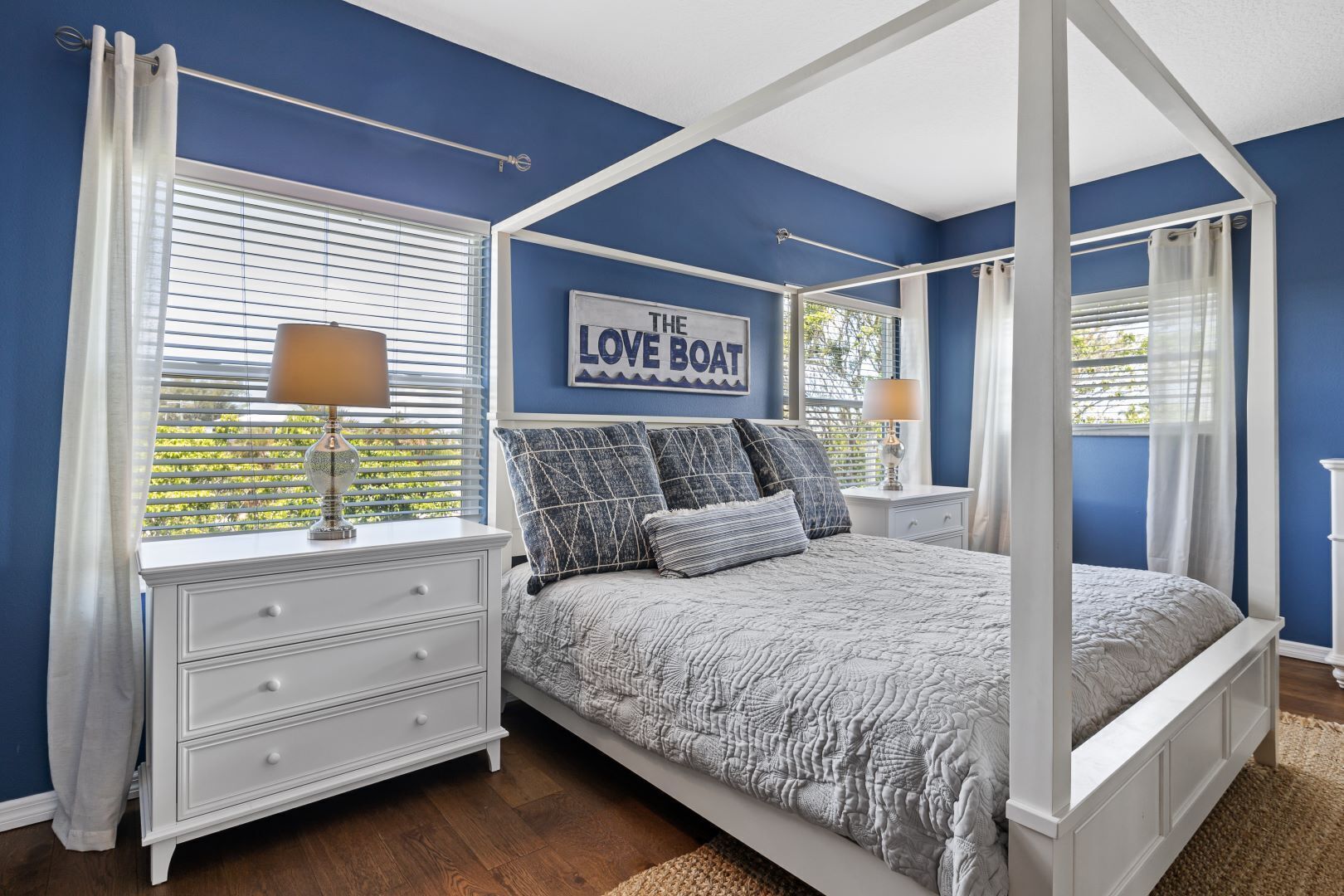 A bedroom with a four-poster bed, a white dresser, and a window with blinds.