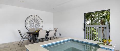 Un área de piscina con bordeado de azulejos, una mesa de comedor con sillas y una obra de arte con forma de brújula.
