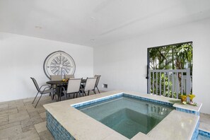A pool area with a tiled edge, a dining table with chairs, and a compass wall art piece.