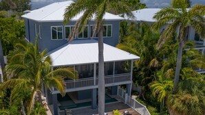 A two-story house with a balcony, a pool, and surrounded by palm trees. - Getaway By The Bay-4 bedrooms-Large private pool and spa across from the bay!! (Bradenton Beach)