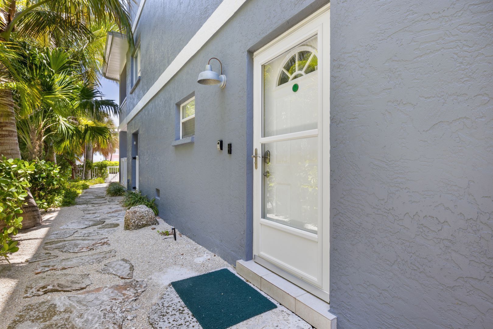 Un bâtiment avec une porte blanche, une petite fenêtre et un luminaire fixé au mur.