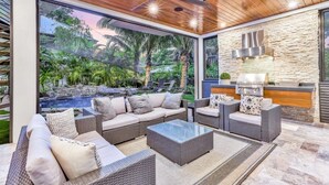 A modern outdoor living area with wicker furniture, a glass-top table, and a stone wall.