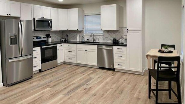 A modern kitchen with white cabinets, stainless steel appliances, and a wooden floor. - Boho 405 - DI Home Rentals (Stillwater)