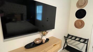 A TV mounted on a wall, a wooden console table with a remote, and three hats on the wall.