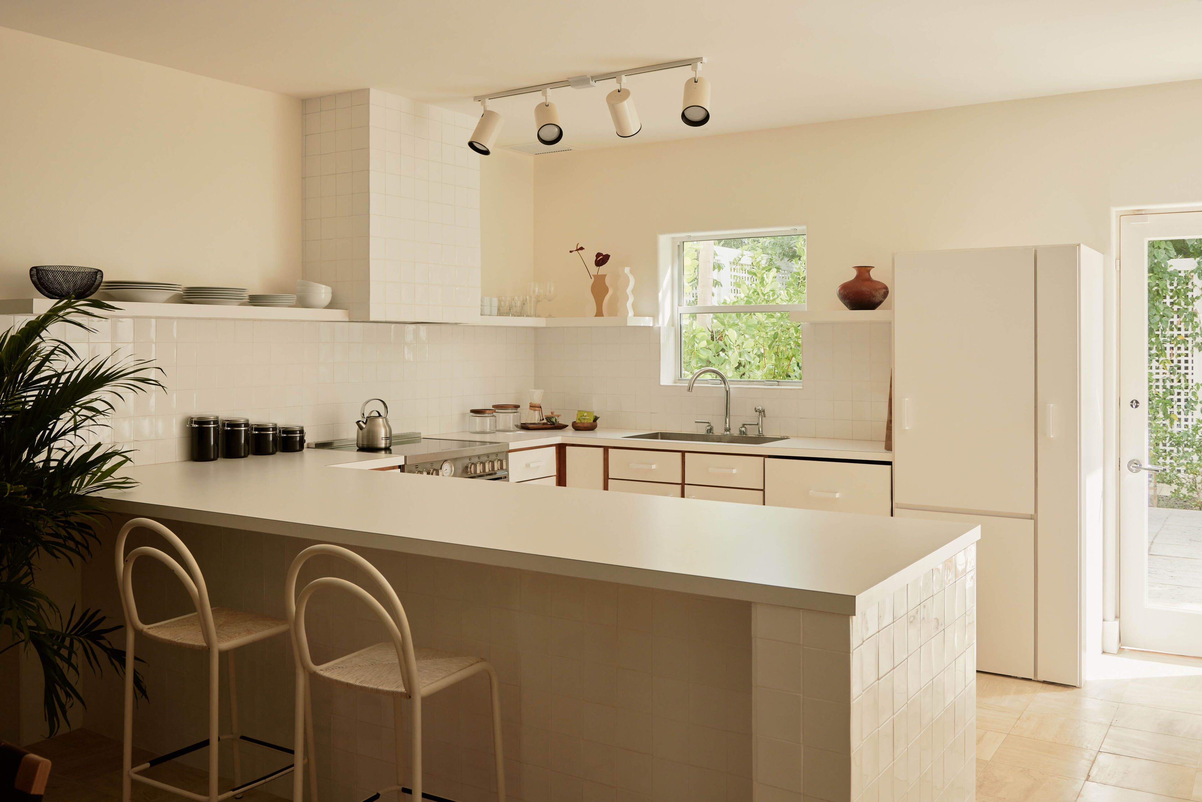 Een moderne keuken met een groot schiereiland, barkrukken, een raam en uitzicht op groen.