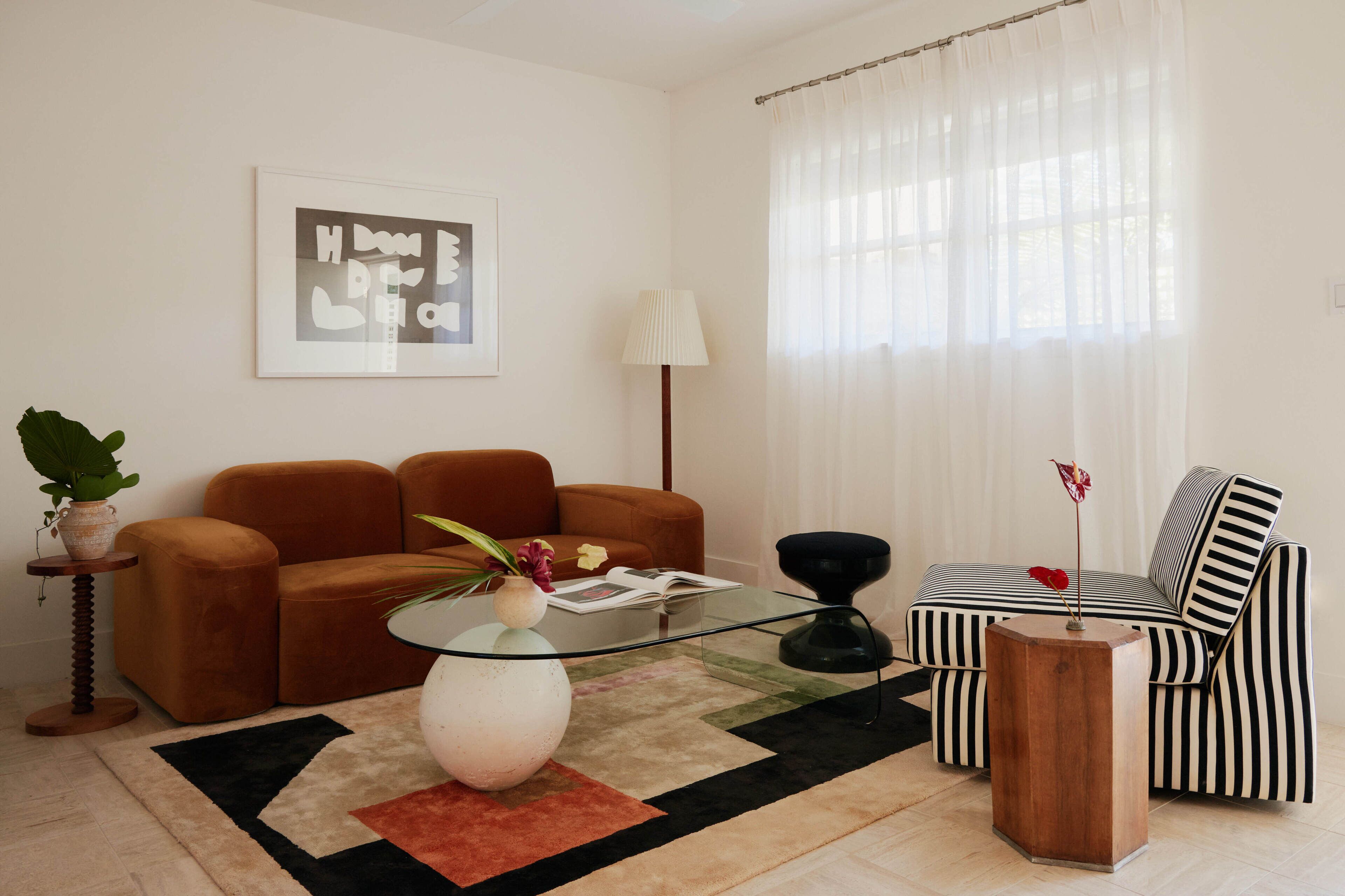 Un salon avec un canapé marron, un fauteuil à rayures, une table basse en verre et un tapis.
