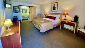 A hotel room with a bed, bedside lamps, a desk with a lamp, a chair, a desk lamp, a coffee maker, a mirror, a picture frame, and a sliding door. - Old Montana Inn (Deer Lodge)