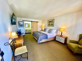 Habitación de hotel con cama, mesitas de noche, escritorio, silla, armario y baño.