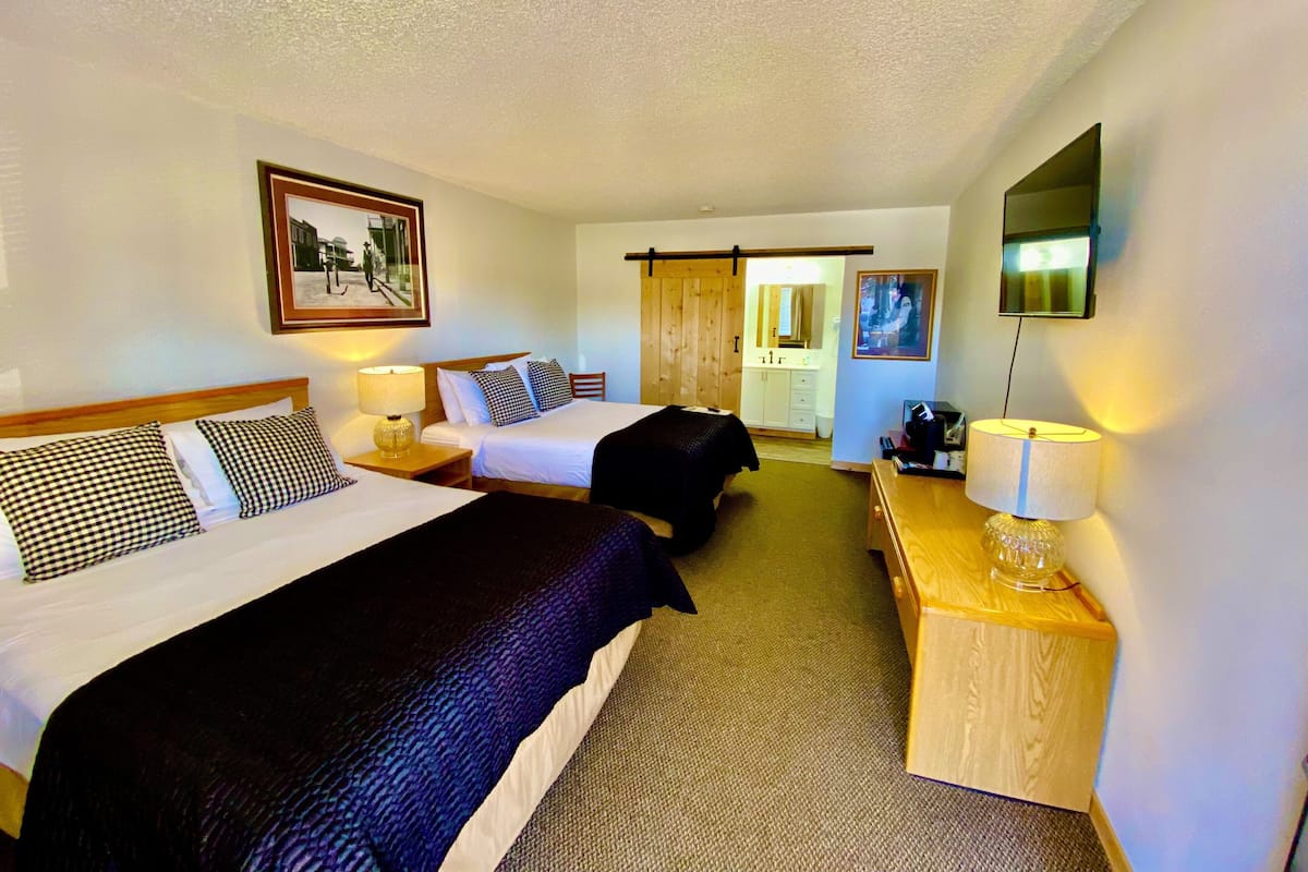 Ein Hotelzimmer mit zwei Betten, einem Schreibtisch, einem Stuhl, einem Fernseher und einem durch eine Schiebetür einsehbaren Badezimmer.