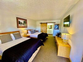 Habitación de hotel con dos camas, un escritorio, una silla, un televisor y un baño visible a través de una puerta corrediza.