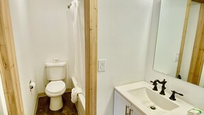 A bathroom with a toilet, sink, and mirror. - Old Montana Inn (Deer Lodge)