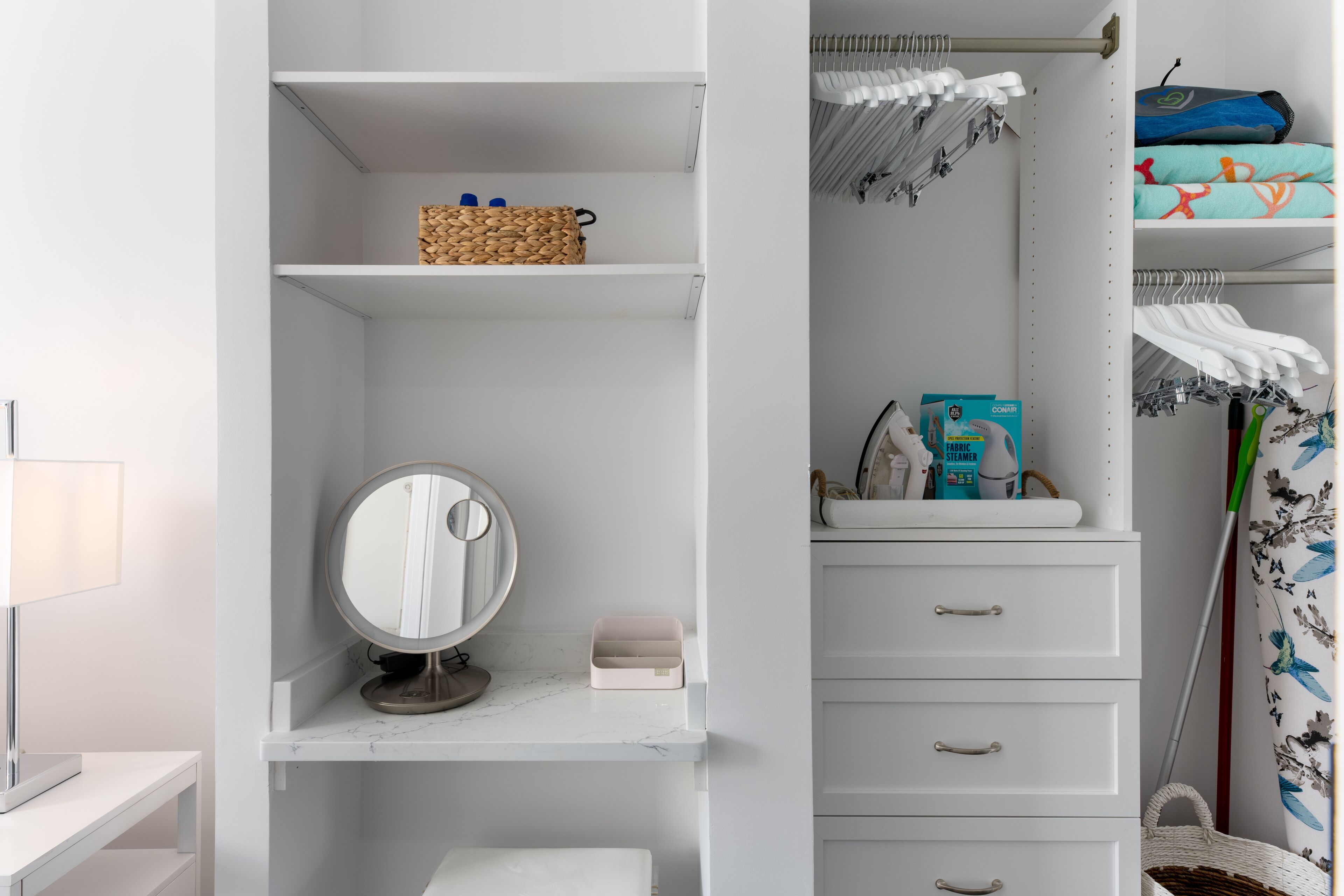 Een witte badkamer met een wastafel, een ronde spiegel, een plank met toiletartikelen en een handdoekhouder.