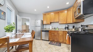 A modern kitchen with wooden cabinets, a black stove, and a dining area with a table and chairs. - North End Studio (Boston)