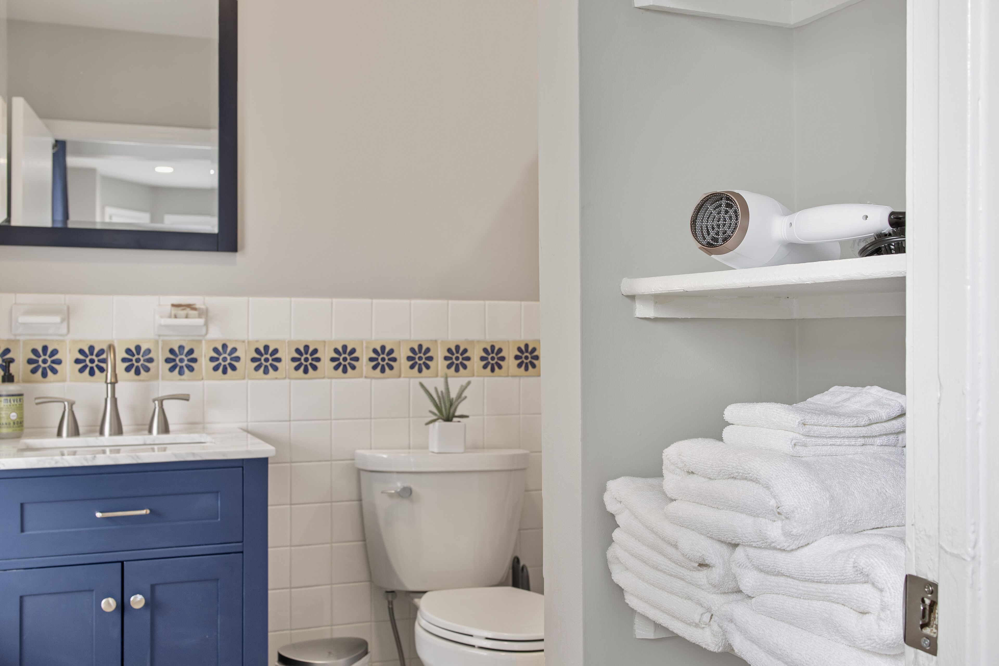 A bathroom with a blue vanity, white toilet, and a towel rack with folded towels.