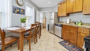 A kitchen with wooden cabinets, a stainless steel refrigerator, and a dining table with chairs. - North End Studio (Boston)