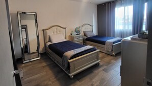 Ein Schlafzimmer mit zwei Betten, einem Deckenventilator, einem Spiegel, einer Kommode und einem Fenster mit Vorhängen.
