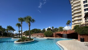 Una piscina con agua cristalina azul, rodeada de palmeras y un edificio con balcones.