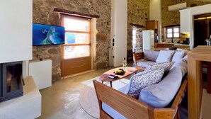 Una sala de estar acogedora con paredes de piedra, un sofá de madera, un televisor y una chimenea.