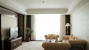 Habitación de hotel con sofá, televisión, planta en maceta y vistas al exterior.