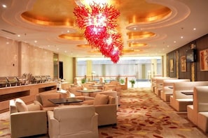 Un hall d’hôtel comprenant des espaces aménagés avec des sièges, un comptoir d’accueil et un grand lustre.