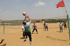 A beach volleyball game with players and a net.