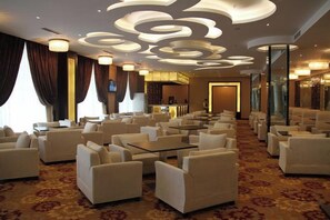 A hotel lobby with rows of white armchairs, a bar area, and a patterned carpet. - Xingyu Tangsuge Desert Hot Spring Hotel (Otog Front Banner)