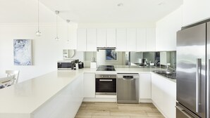 Una cucina moderna con mobili bianchi, elettrodomestici in acciaio inossidabile e luci a sospensione.