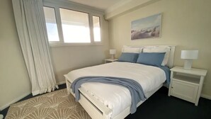 Una camera da letto con un letto, comodini, una finestra con tende, un quadro appeso e un tappeto decorato.