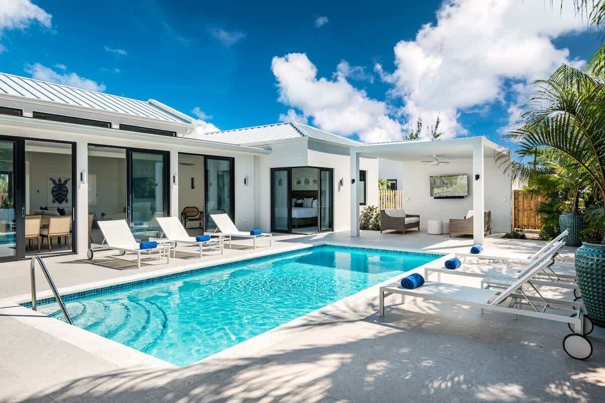 A modern house with a swimming pool, lounge chairs, and a patio area.