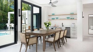 Une cuisine moderne avec des meubles blancs, une table à manger avec des chaises et une vue sur une piscine.