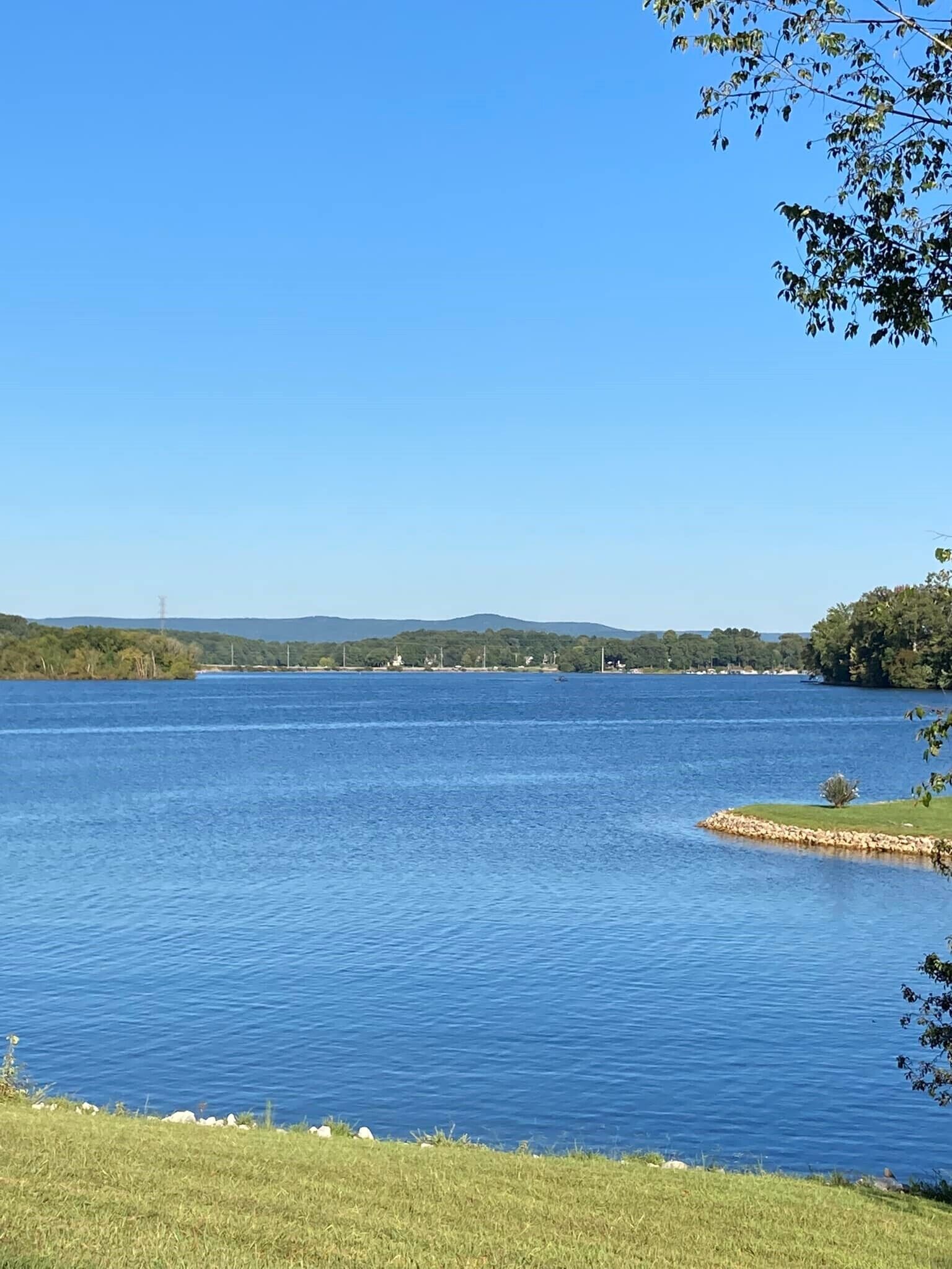Un lago tranquilo con cielo despejado, rodeado de vegetación y colinas al distante.