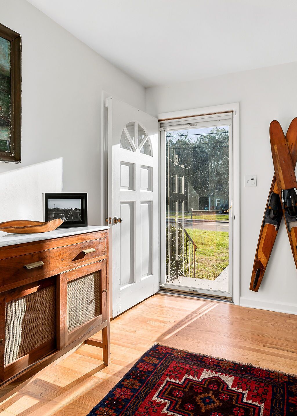Une pièce avec un meuble en bois, une porte donnant sur l’extérieur et des skis appuyés contre le mur.