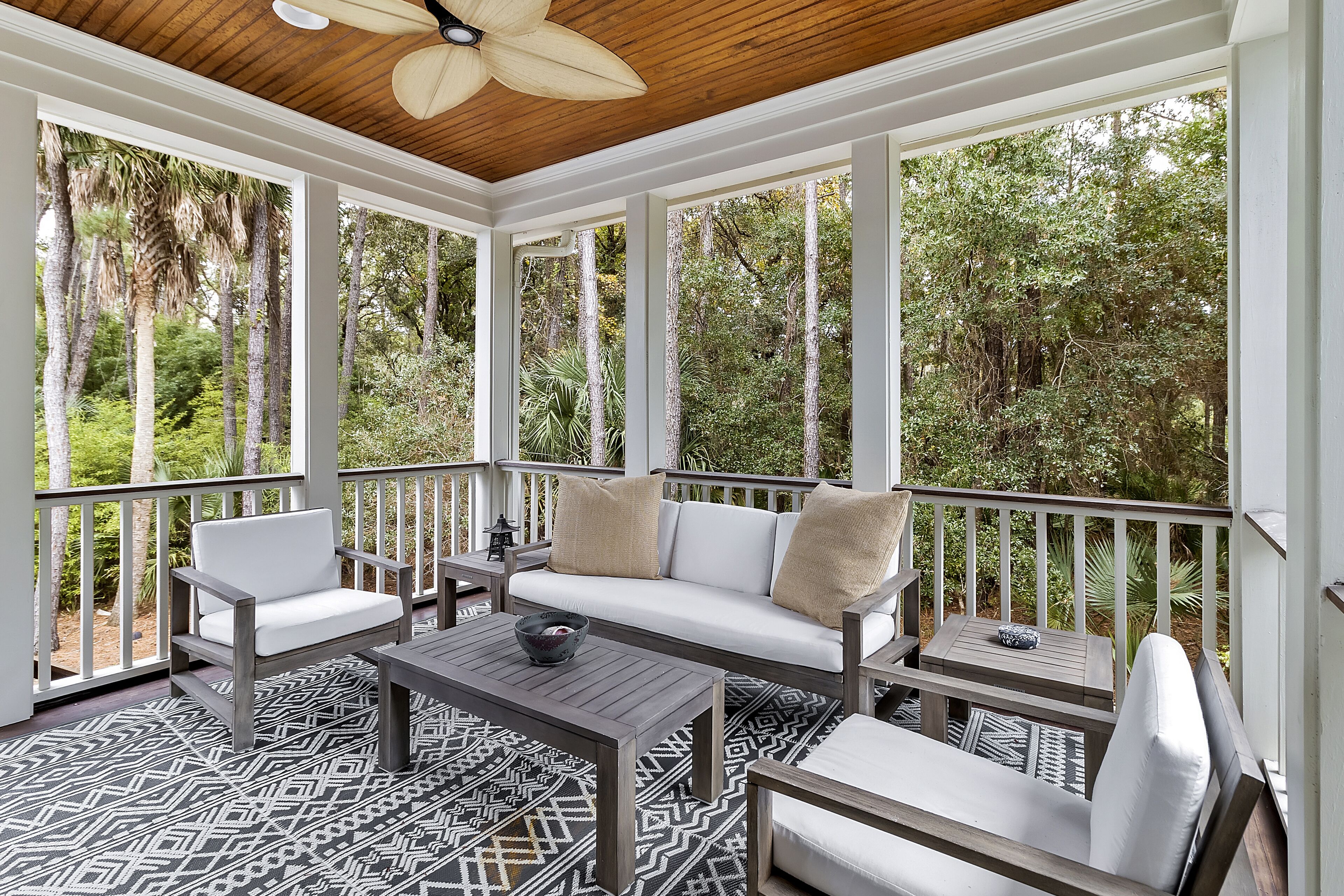 A covered porch with a wooden ceiling, white-framed windows, and a patterned floor.