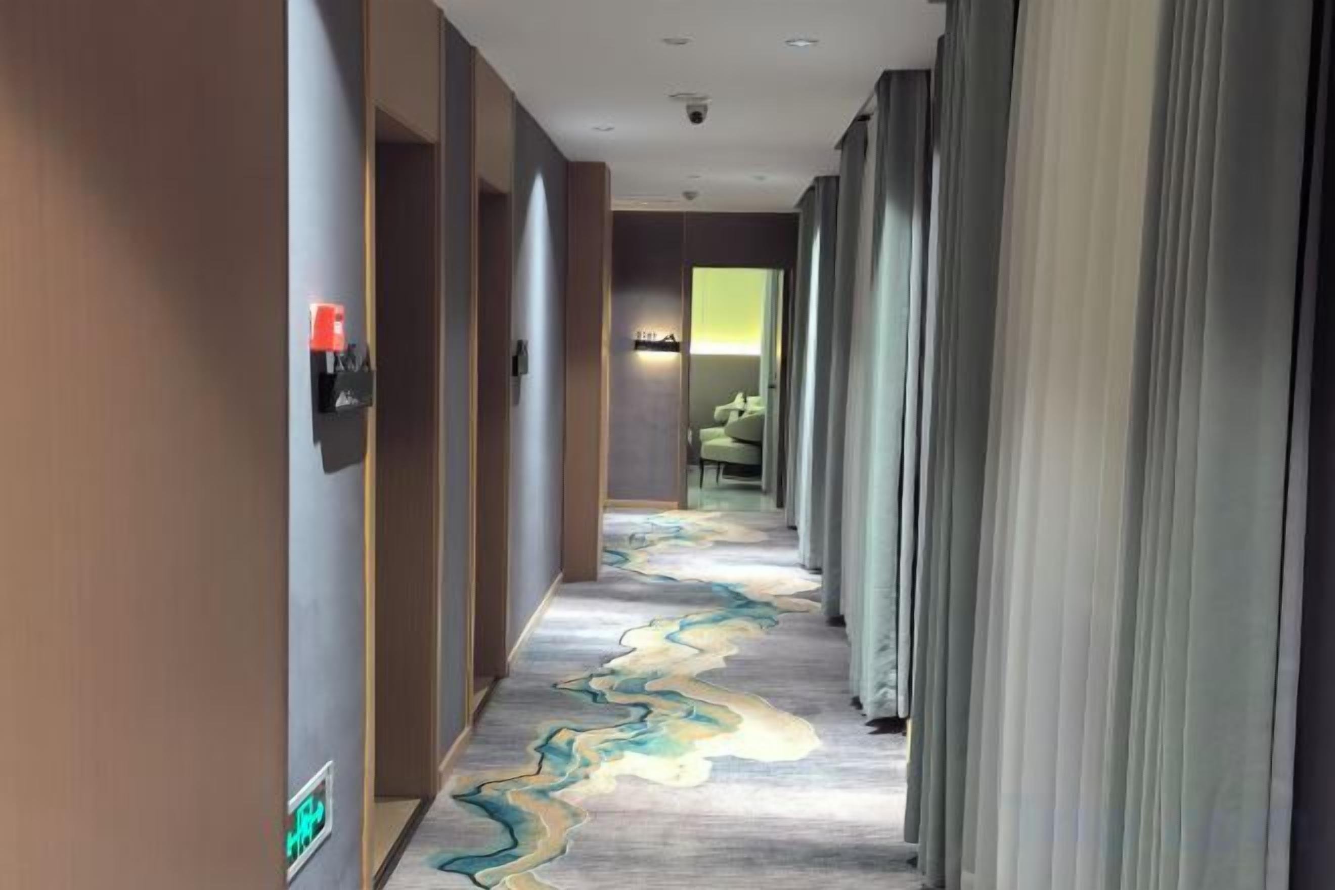 Un couloir d’hôtel avec un tapis à motifs, un comptoir de réception et un espace détente avec des fauteuils.