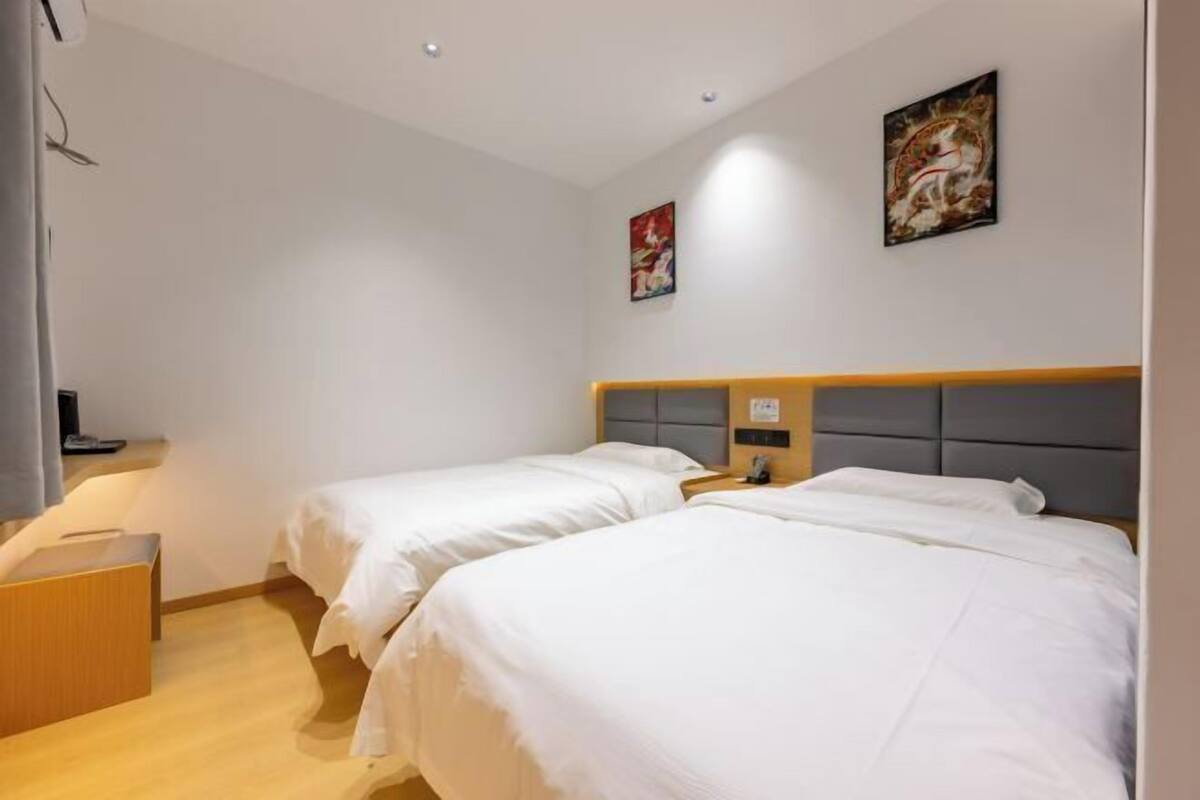 Une chambre d’hôtel avec deux lits simples, une table de chevet en bois, une petite table et un téléviseur fixé au mur.
