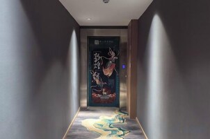 Un pasillo con una puerta que presenta una obra de arte tradicional, una alfombra estampada y un ascensor moderno.