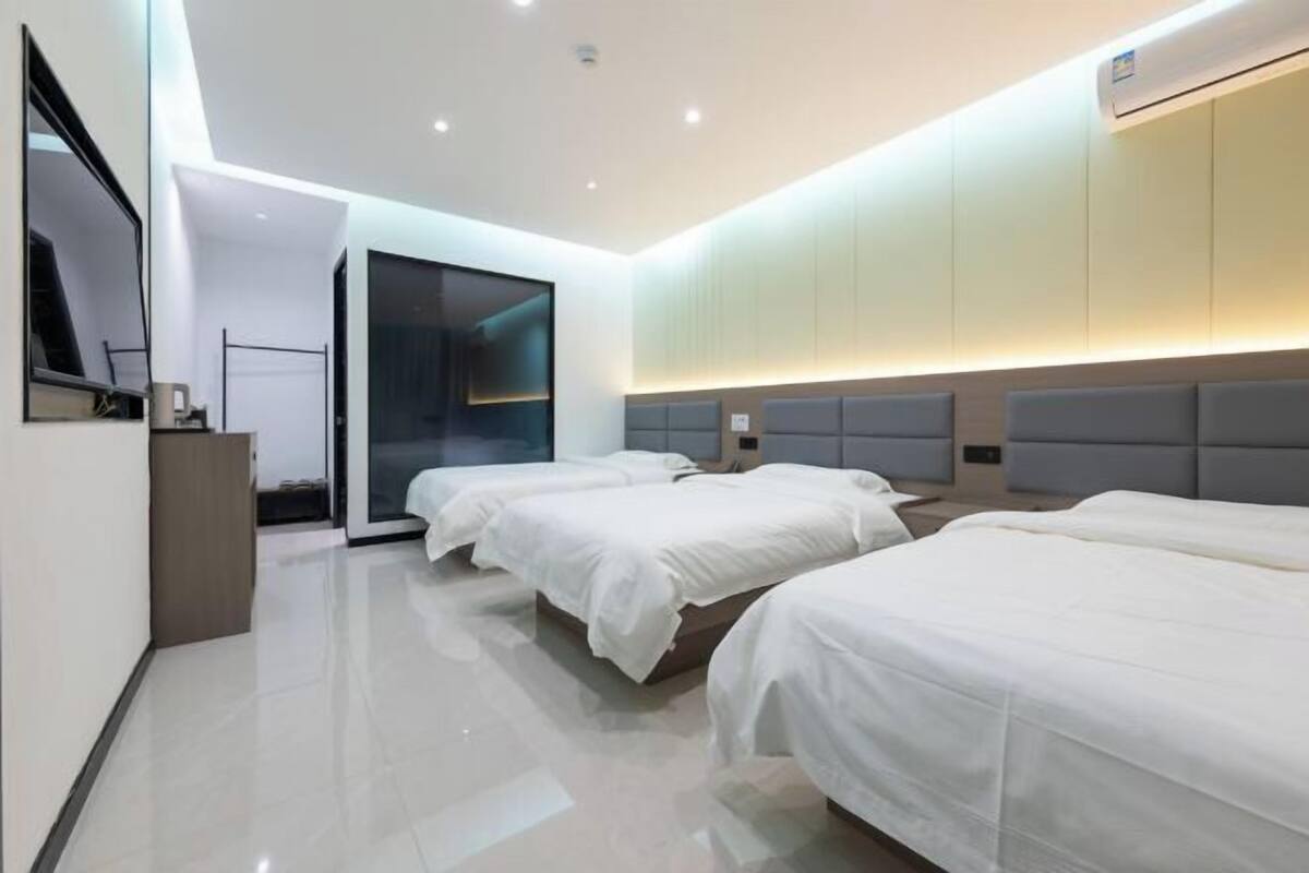 Une chambre d’hôtel moderne avec trois lits, un grand miroir et une porte coulissante donnant accès à la salle de bain.