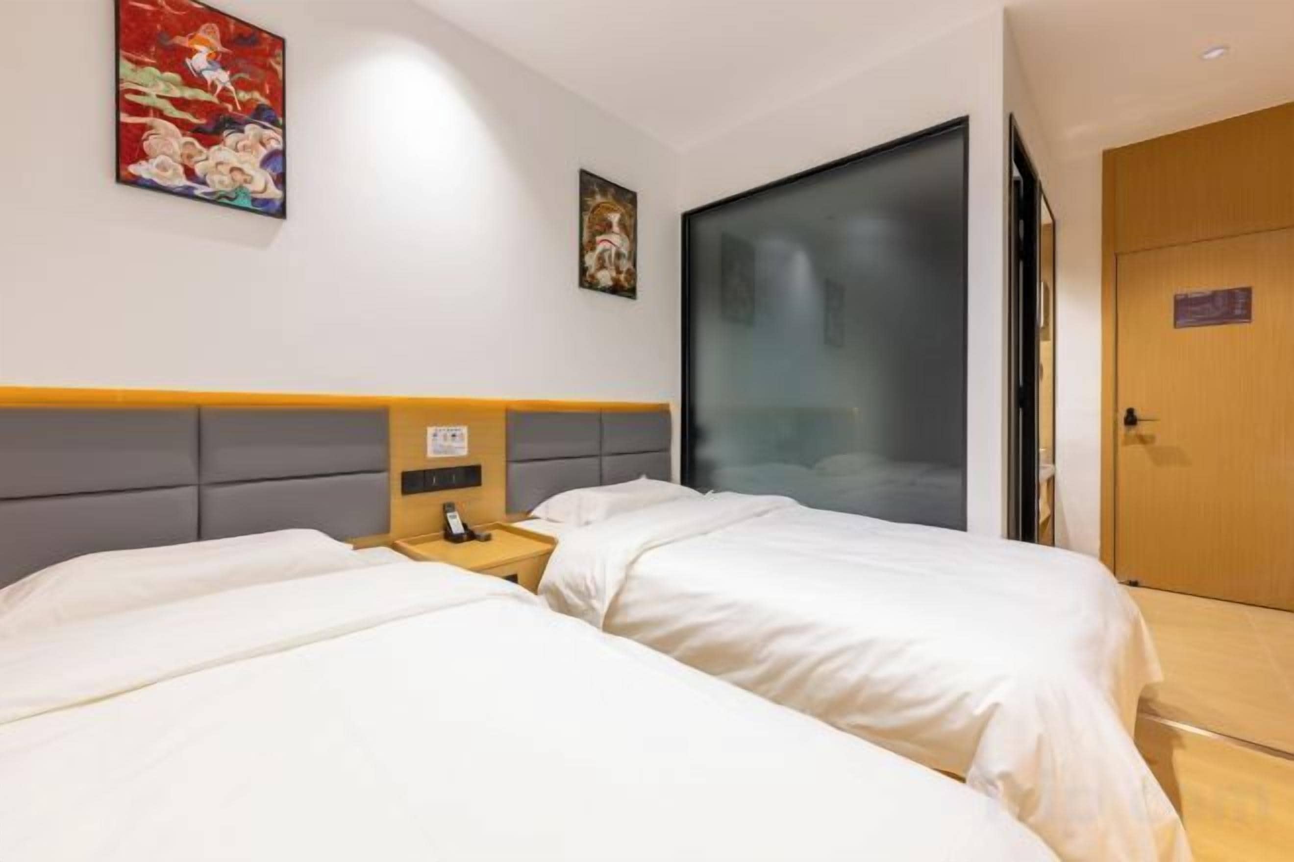 A hotel room with two beds, a bedside table with a phone, and a door with a sign.