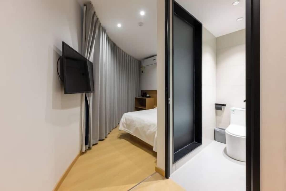 Une chambre d’hôtel moderne équipée d’un lit, d’un téléviseur fixé au mur, d’une salle de bain avec des toilettes et un lavabo, et d’un plancher en bois.