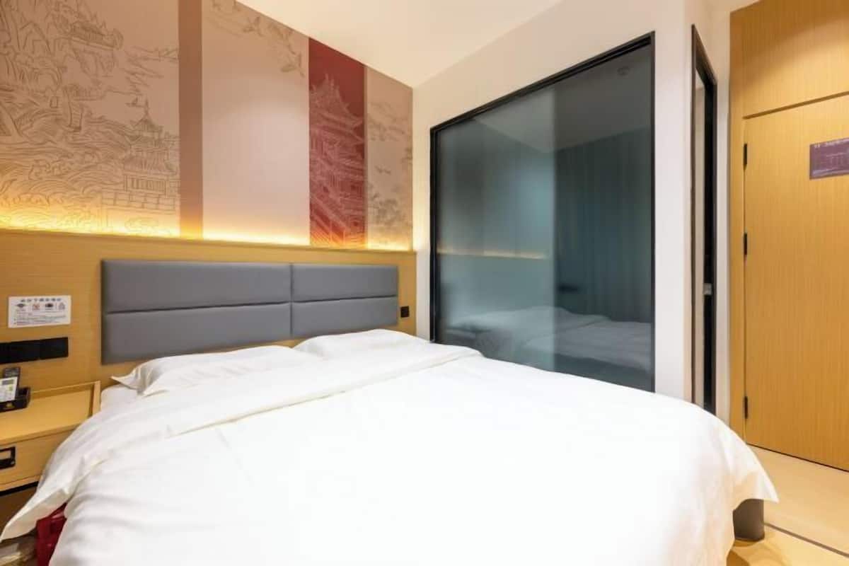 Une chambre d’hôtel comprenant un lit, une table de chevet, un mur décoré d’œuvres d’art, une porte coulissante et une porte en bois.