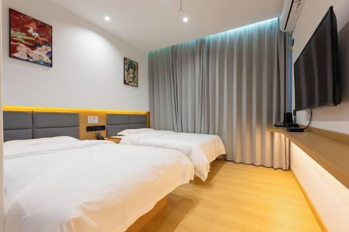 Une chambre d’hôtel avec deux lits, un téléviseur à écran plat, un tableau au mur et une fenêtre avec des rideaux.