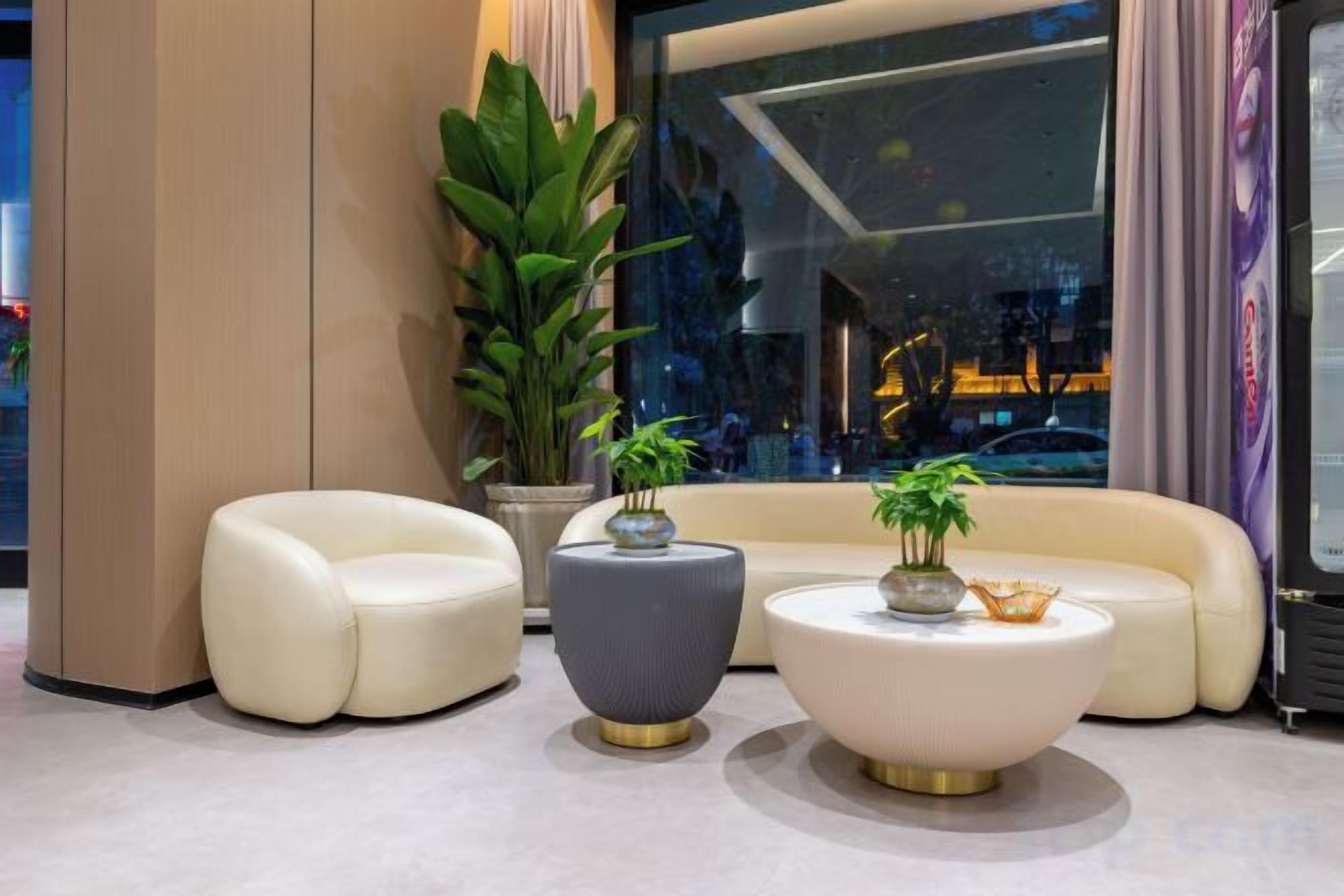 A modern lounge area with a sofa, two round tables, and a potted plant.