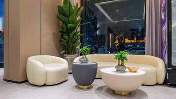 A modern lounge area with a sofa, two round tables, and a potted plant.