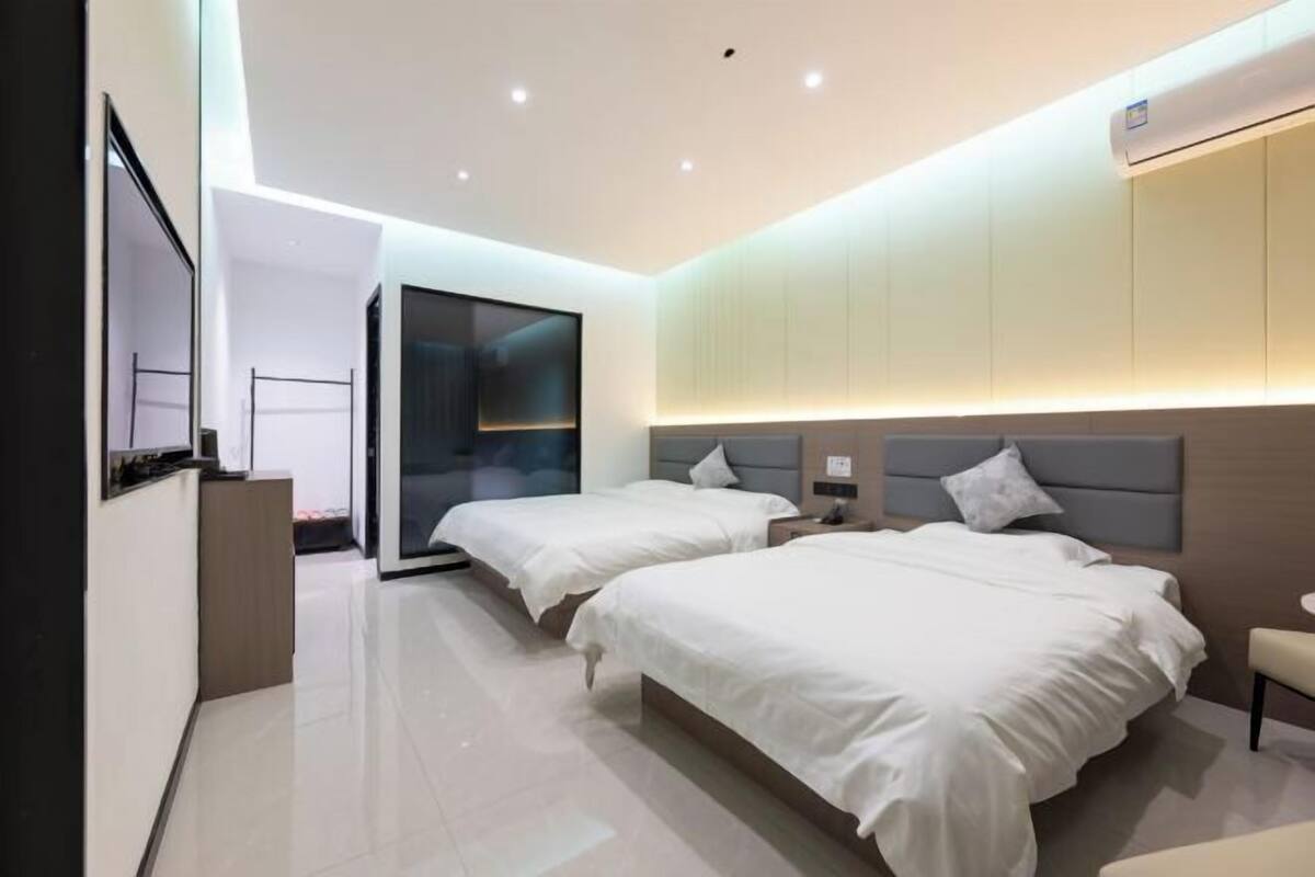 Une chambre d’hôtel moderne équipée de deux lits, d’une télévision, d’un bureau et d’une porte coulissante donnant accès à la salle de bain.
